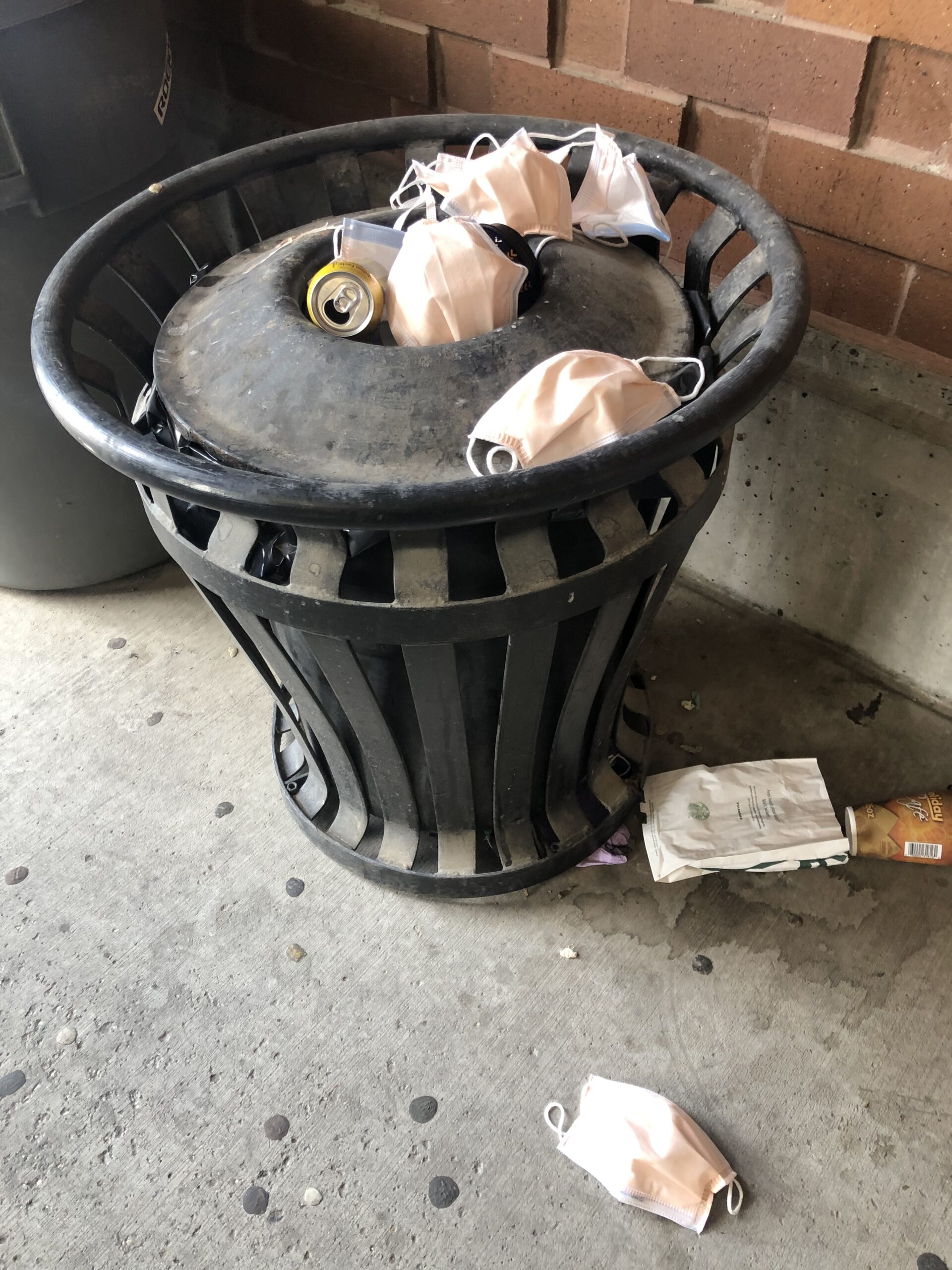 A photo of a trash bin that is overflowing with garbage, primarily N95 masks.