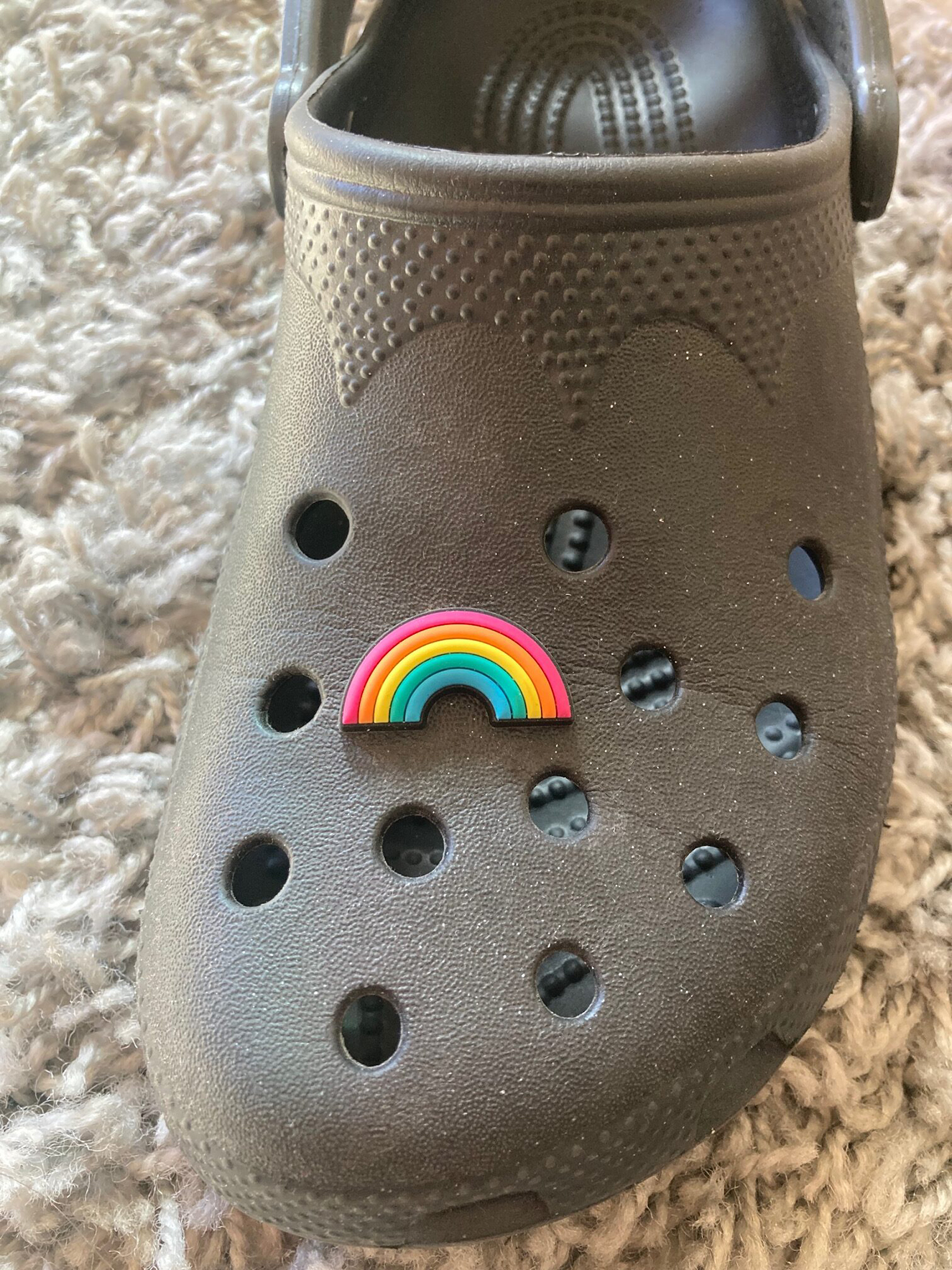 A black croc shoe with a rainbow charm