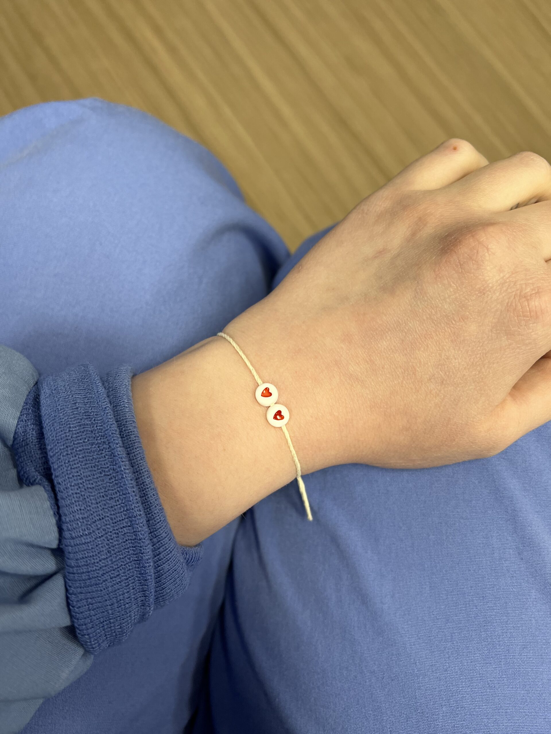A person in scrubs wearing a bracelet on their wrist that has two charms with hearts on it.