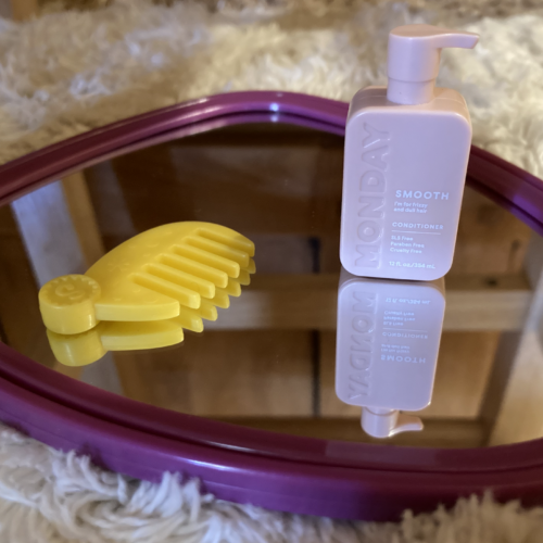 A photo of a small comb and bottle of conditioner on top of a mirror with a purple frame