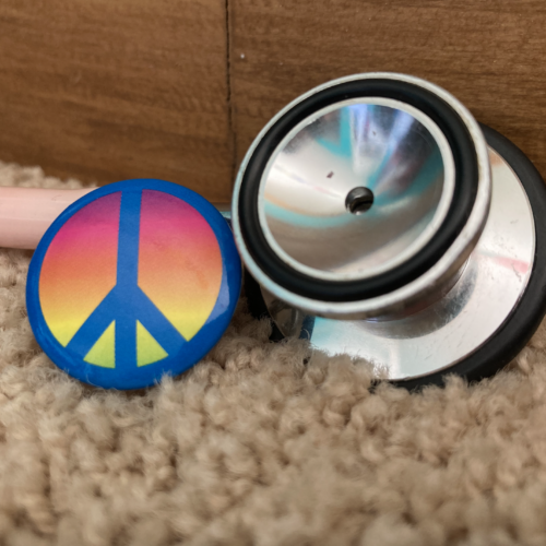 A photo of a stethoscope and a button with a rainbow-colored peace sign