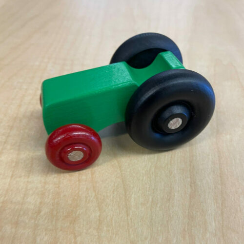 a photo of a small green toy tractor, made out of wood, with red and black wheels.