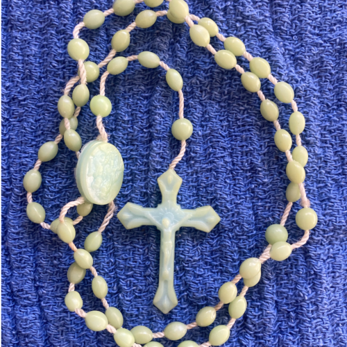 A Rosary with light green beads and cross placed on top of blue cloth