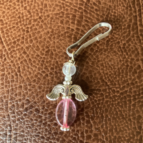 A photo of a small earring with a pink bead and angel wings