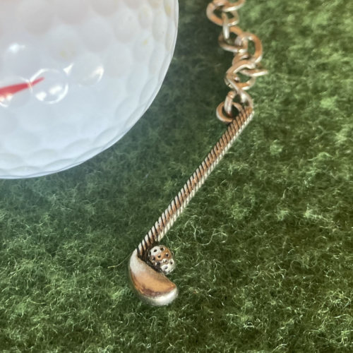 Photo of a golf ball and a small, gold golf club pendant