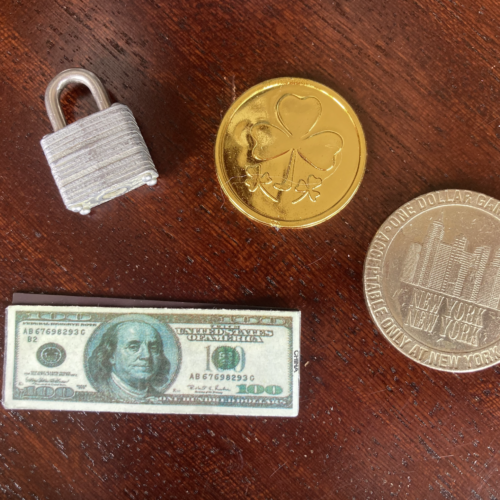A photo of a small lock, token, shamrock coin, and mini $100 bill